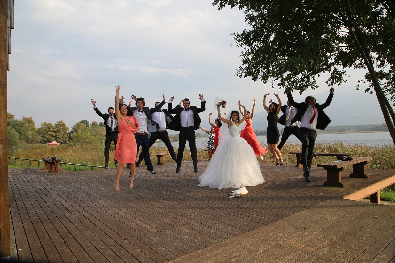 bride, groom, and guests jump for joy with a cat in the foreground