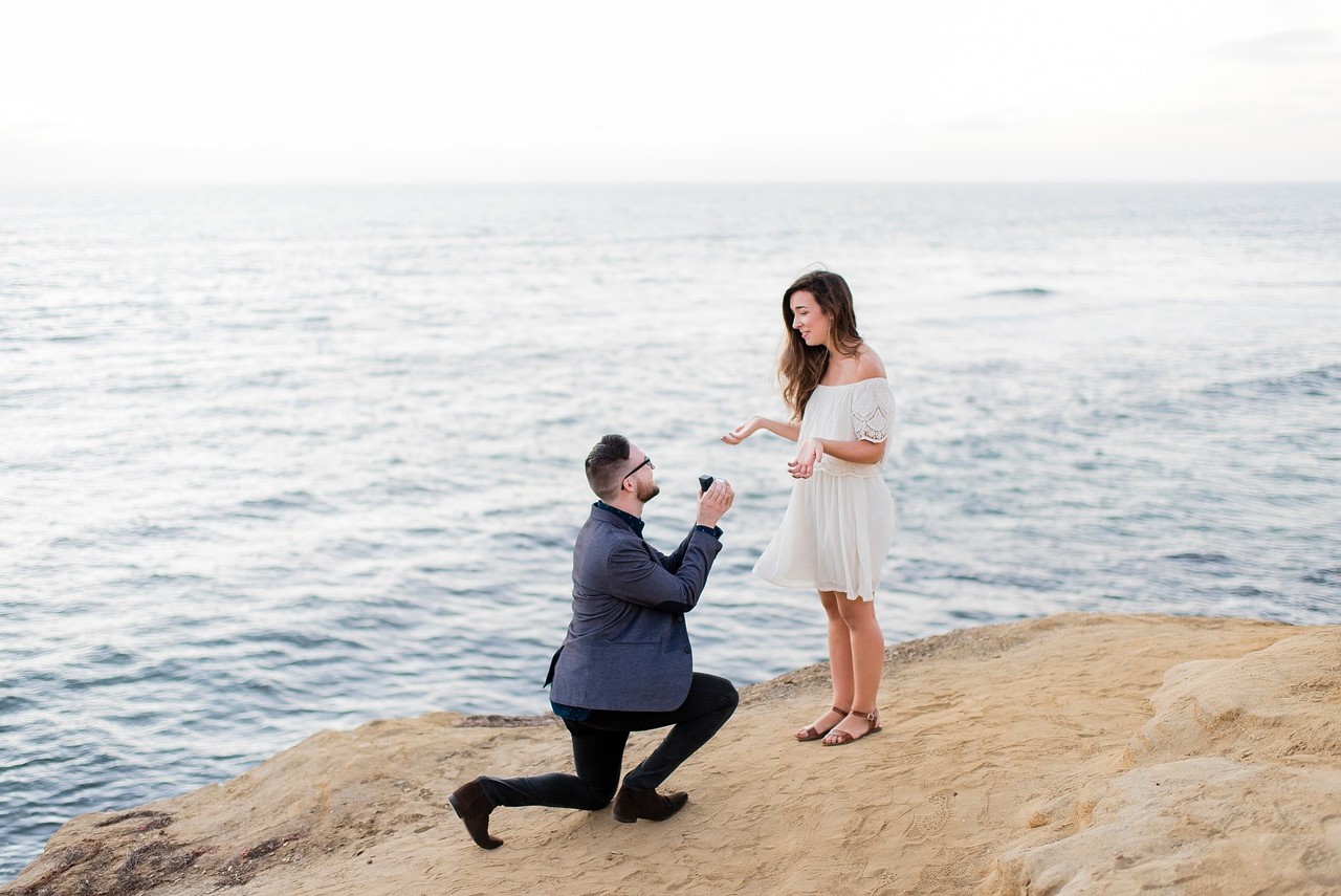 By the water, he proposes to her on bended knee.