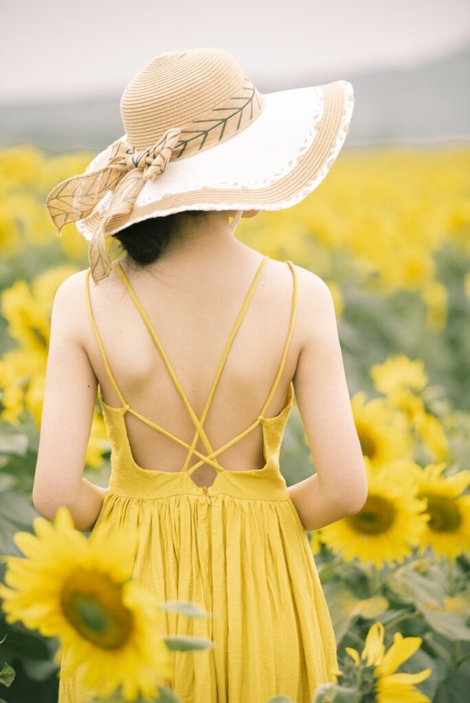 woman in a yellow sundress and hat surrounded by sunflowers Pixabay.com
