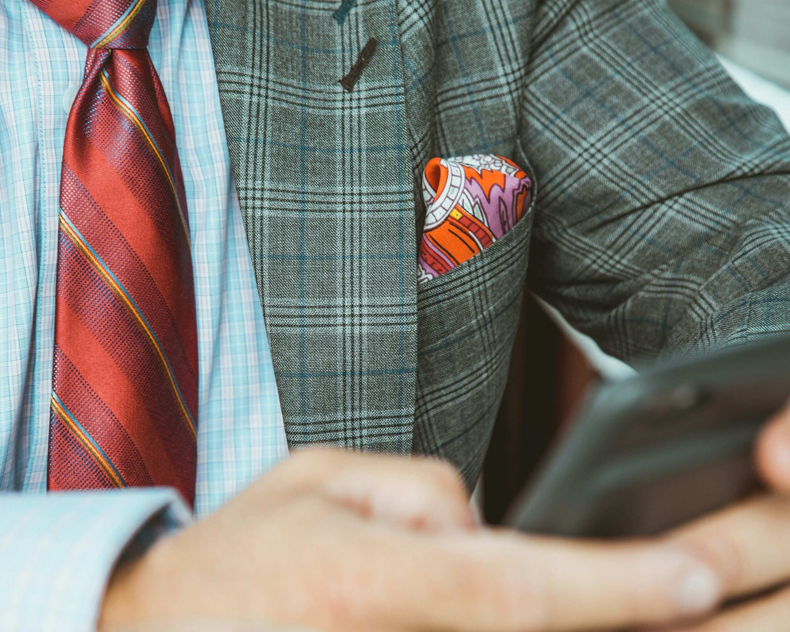 man in a gray check suit with a red tie and pocket square Unsplash