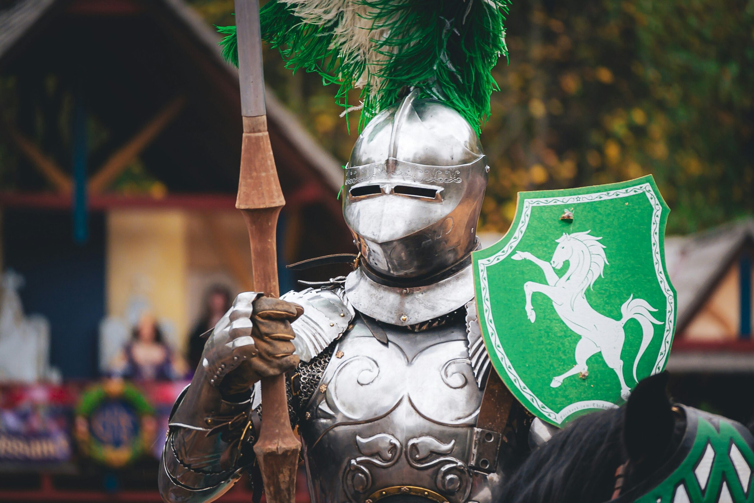 A knight in silver armor holds a lance and a shield with a green background and a white horse rampant. Unsplash.com