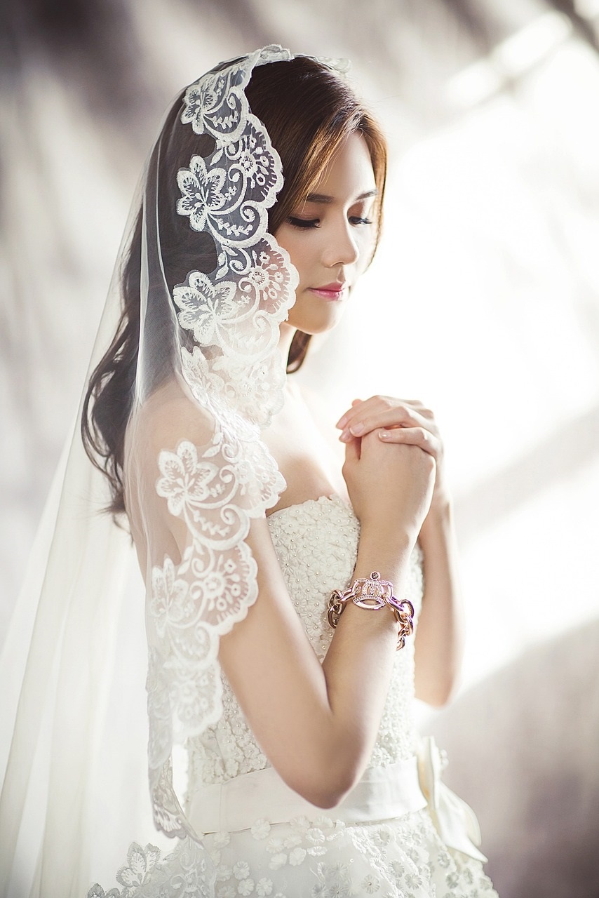 With hands clasped in prayer, bride wears lace trimmed veil Pixabay