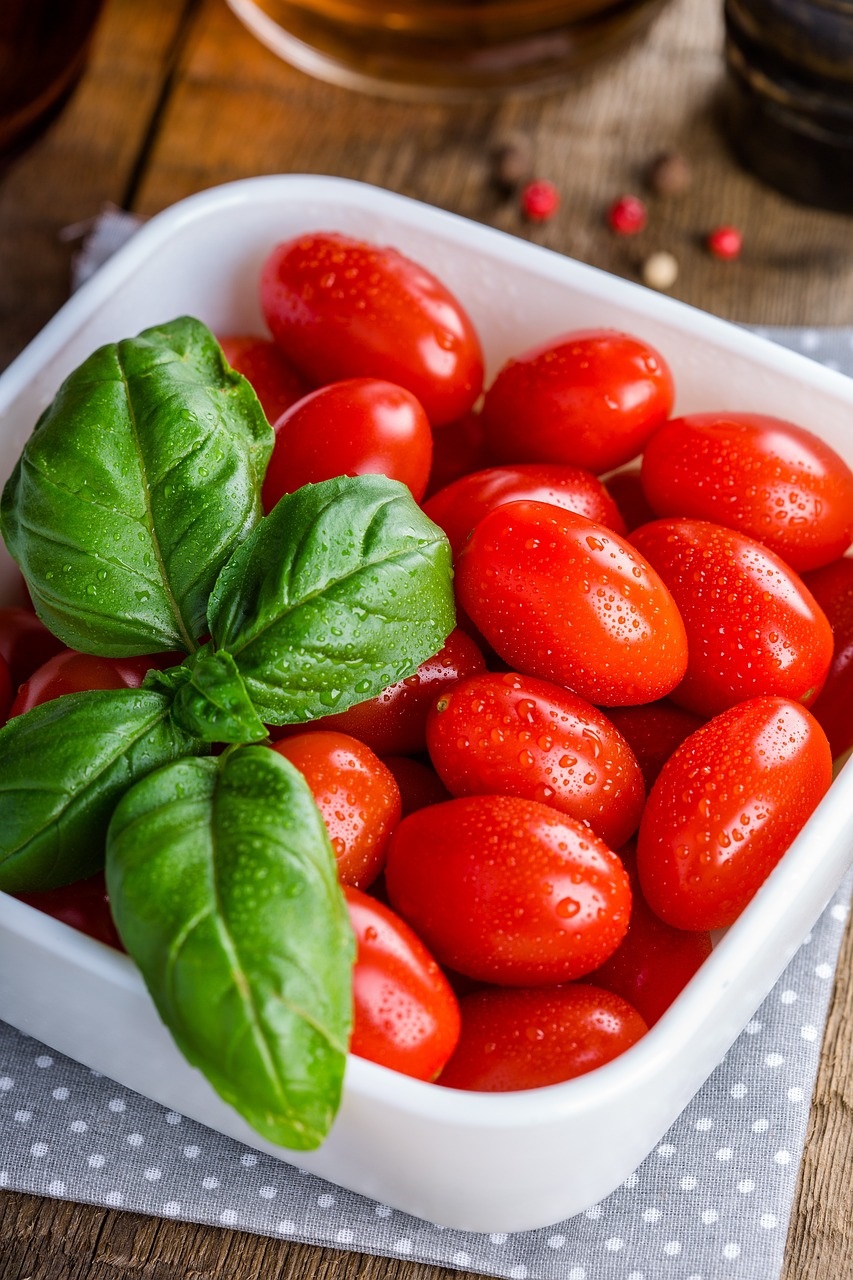 A white rectangular bowl is filled with red ripe tomatoes and fresh green basil