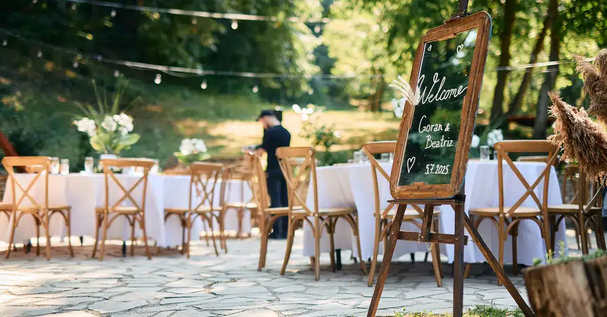Outdoor wedding reception setup with welcome sign, wooden chairs, and string lights