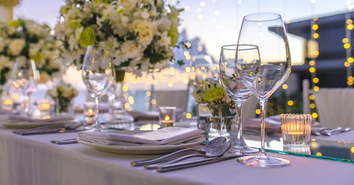 Elegant outdoor wedding reception table with candles, floral centerpieces, and glassware at dusk