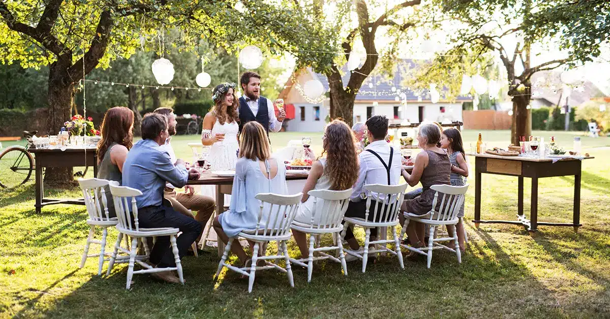 Outdoor wedding reception with guests dining beneath string lights and trees