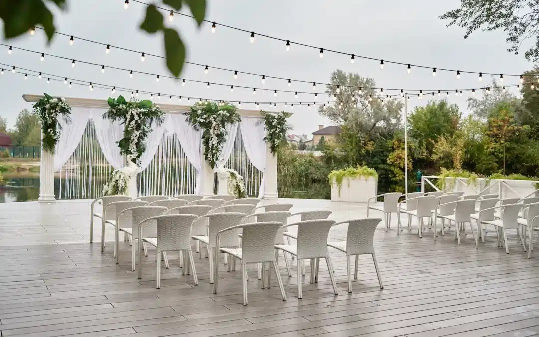 Outdoor wedding ceremony setup beside lake with floral arch and string lighting